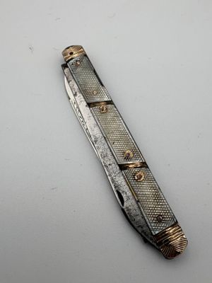un couteau de poche argenté et doré posé sur une surface blanche