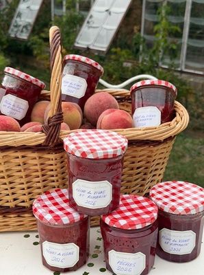 de nombreux pots de confiture posés sur une table, avec un panier de pêches en arrière-plan
