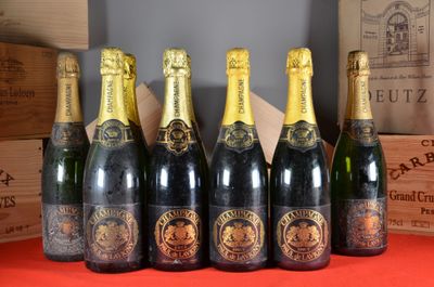 six bottles of champagne lined up on a table with boxes in the background