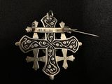 an image of a silver cross pin with a ribbon on a black background
