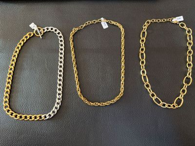 trois colliers à chaînes en or posés sur une surface en cuir noir