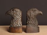 une paire de serre-livres en bronze représentant des têtes d'aigle, posés sur une table en bois
