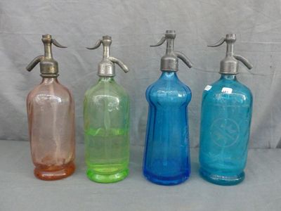 quatre bouteilles en verre de couleurs différentes, munies d'un bec verseur en métal, posées sur une table