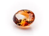 a close up of an orange sapphire stone on a white surface