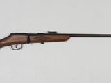 un gros plan d'un fusil posé contre un mur blanc, avec une crosse en bois