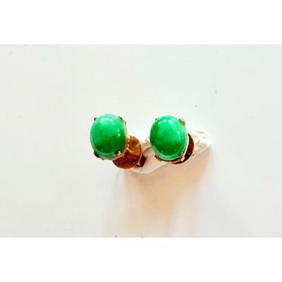 une paire de boucles d'oreilles à clous ornées de pierres vertes, posées sur une surface blanche