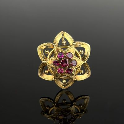 an image of a gold ring with pink stones on a black surface