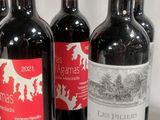 four bottles of red wine are lined up on a table
