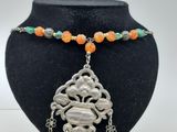 un collier avec un pendentif en argent et des perles orange sur un mannequin noir