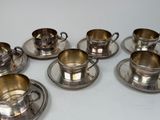 six silver plated cups and saucers on a white surface