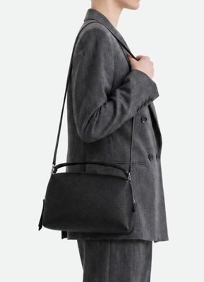 Une femme en tailleur gris tient un sac noir.