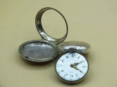 a silver pocket watch sitting on a table next to a ring