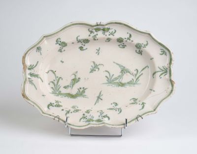 une assiette verte et blanche posée sur un support, sur une surface blanche