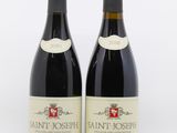 two bottles of red wine sitting next to each other on a white surface