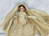 une vieille poupée allongée sur un drap blanc avec un voile sur la tête