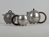 two silver teapots and a coffee pot on a white surface
