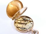 a gold pocket watch that is open on a white surface
