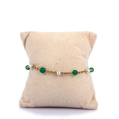 un gros plan sur un oreiller posé sur un autre oreiller, avec un bracelet vert en perles