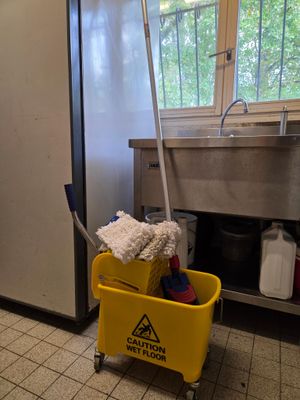un seau jaune avec une serpillière accrochée dessus, dans une cuisine