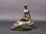 une statue en bronze d'une femme assise sur un rocher