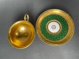 two gold and green cups and saucers on a table