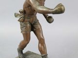 statue en bronze représentant un garçon portant un gant de boxe, posée sur un socle en bois