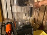 a blender sitting on a table with a person ' s hand on it