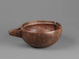 a close up of a wooden bowl with a handle on a gray surface