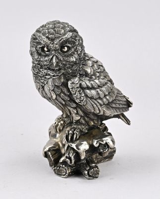 une figurine de chouette en argent posée sur une souche d'arbre