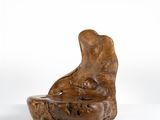 sculpture en bois représentant un chien tenant un bol dans la gueule, posée sur une surface blanche