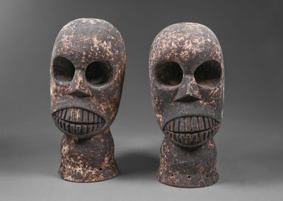 deux masques en bois sculptés représentant des visages, sur fond gris
