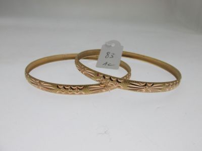 two gold bang bracelets with engraved designs on them