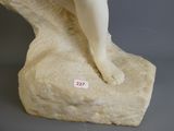 une statue représentant une femme assise sur un rocher, posée sur un fond gris