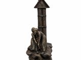 une statue représentant un homme assis sur un rocher, près d'un phare