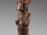 une statue en bois représentant un homme tenant un chat, posée sur un socle noir