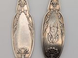 two silver spoons with designs on them sitting next to each other