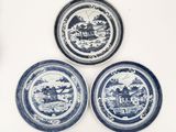 three blue and white plates with a picture of a village on them