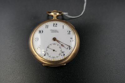 une montre de poche en or avec une chaîne, posée sur un fond noir