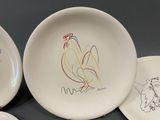 three white plates with drawings of roosters on them sitting on a table