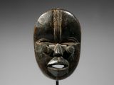 un masque en bois au visage noir, posé sur un socle