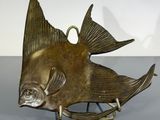 sculpture de poisson en laiton posée sur un socle, sur une surface grise avec un fond blanc