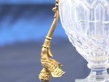 a glass vase with a gold handle and a bird on it