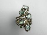 a close up of a ring with green stones on a white surface