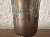 a silver cup on a wooden table with a white wall in the background