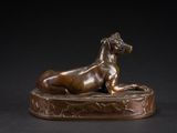 bronze statue of a dog laying down on a base on a black background