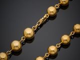 a gold necklace with a ball chain on a black background