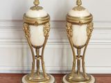 une paire de vases blancs et dorés posés sur le parquet d'une pièce