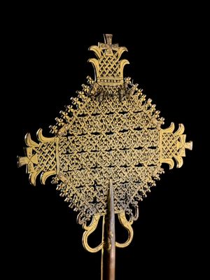 une croix en or richement décorée, fixée sur un bâton en bois, sur fond noir