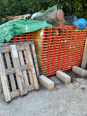 un tas de palettes en bois posé par terre à côté d'une clôture
