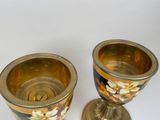 two gold cups with flowers on them on a white surface